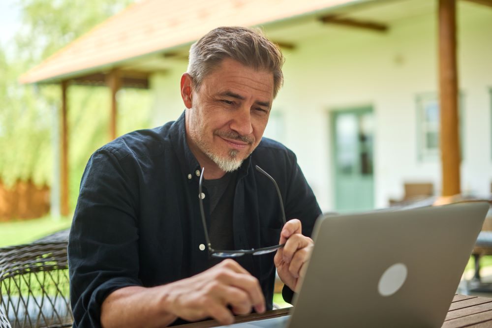 Middle aged man working with laptop computer at home outdoor in garden